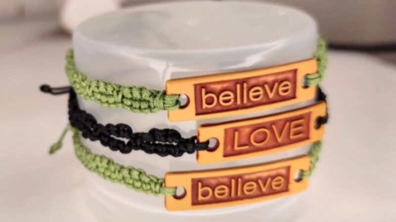 Image of woven bracelets in green and black colors, featuring metallic tags with the words "believe" and "LOVE" engraved on them