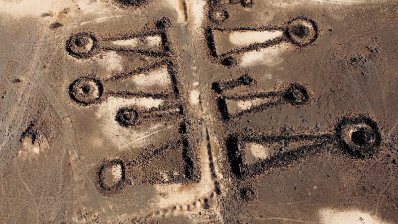 Aerial view of ancient mustatil stone structures in the Saudi Arabian desert, featuring long rectangular shapes with circular ends.